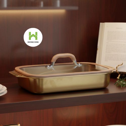 Gold baking dish with a glass lid on a wooden surface, featuring the Homecore logo.